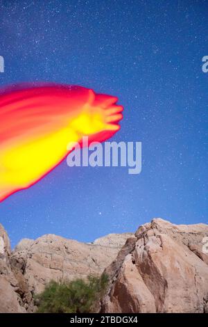 Arms reaching and waving in red light taken with a starry desert landscape in the background. Stock Photo