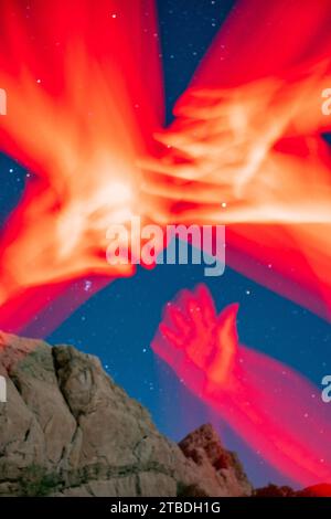 Arms reaching and waving in red light taken with a starry desert landscape in the background. Stock Photo