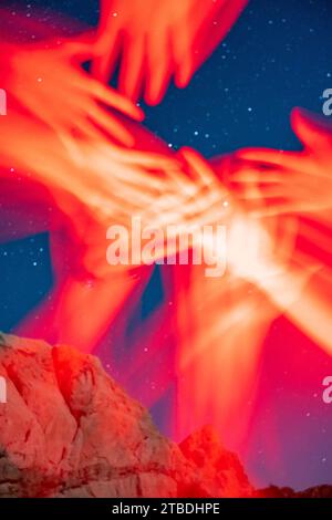 Arms reaching and waving in red light taken with a starry desert landscape in the background. Stock Photo