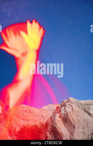 Arms reaching and waving in red light taken with a starry desert landscape in the background. Stock Photo