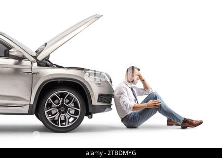Stressed young man sitting next to his broken car isolated on white background Stock Photo