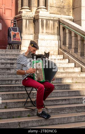 Paris, France - September 01, 2023: Street musician plays accordion with black cat on the stairs of Sacre Coeur Basilica in Montmartre Stock Photo