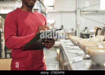 Close up of unrecognizable coffee expert taking notes on clipboard during cupping process in workshop, copy space Stock Photo
