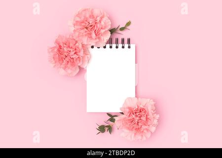 Clean notepad mock up, carnation flowers and green eucalyptus branches on a pink background. Springtime holidays concept. Stock Photo