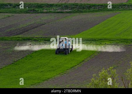Aerial view of tractor spraying crop in green farm fields with pesticide. Stock Photo