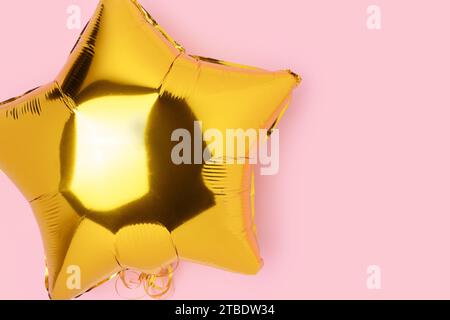 Big gold colored inflatable foil balloon in a star shape. Festive concept on a pink pastel background. Stock Photo