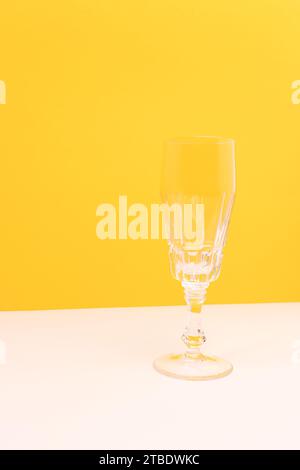 Empty crystal glass in front of yellow background. Place for your design. Stock Photo
