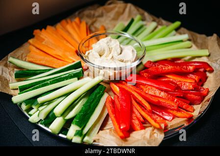 Vegetables cut into strips: cucumber, red bell pepper, carrots, celery and hummus in a glass bowl. Stock Photo