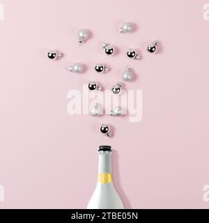 White champagne bottle with Christmas baubles decorations on pink background. Minimal New Year or Christmas concept. Stock Photo
