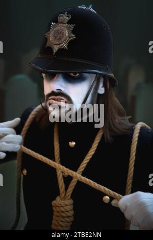 A close up portrait of a male cosplayer at a comic con event in a scary British Police uniform with white painted face in a Halloween concept Stock Photo