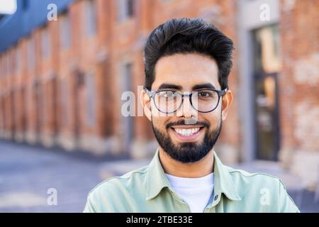 Close-up portrait of a young Hindu man standing on the street near a building, smiling widely and looking at the camera Stock Photo