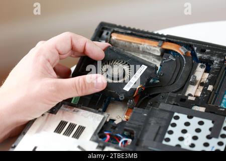 Fixing laptop. Repairman holds cooling fan and repairs from overheating. Disassembling computer, replacement, clean dust and dirt cooling system on no Stock Photo