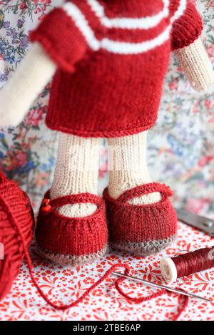 Cute knitted teddy bear toy - amigurumi handcraft with knitting tools and wool (focus on shoes to show handcraft details.) Stock Photo