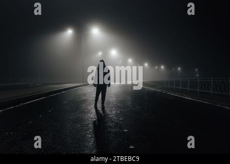 Sad man alone walking along the alley in night foggy road Stock Photo