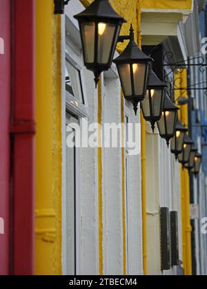 line of brightly painted facades of blue, yellow & red with white window frames beneath old-fashioned lanterns on seaside frontage Stock Photo