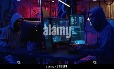Hackers in dark abandoned warehouse using phishing technique that tricks users into revealing sensitive information. Rogue developers stealing passwords from low security systems, dolly in shot Stock Photo