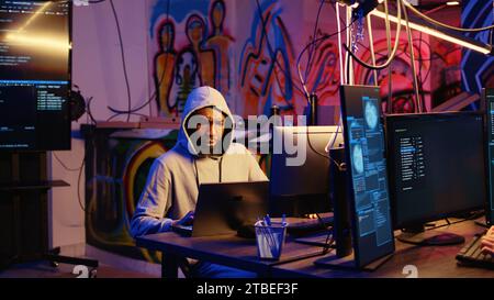 Hacker arriving with laptop in hidden base, deploying viruses on unaware victims computers, stealing sensitive and private information, selling it on darknet black market to highest bidder Stock Photo