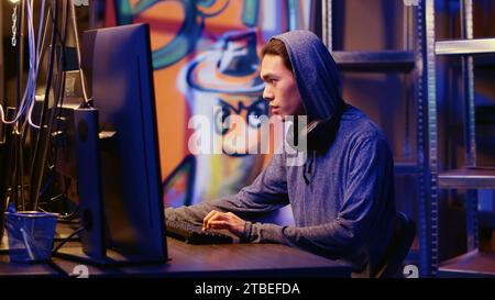 Happy asian hacker in graffiti painted hideout having burst of joy after managing to steal valuable data, using phishing technique that tricks users into revealing sensitive information Stock Photo