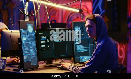 Rogue programmer in graffiti sprayed hideaway targeting vulnerable unpatched connections, focused on getting past digital devices security and stealing valuable sensitive data Stock Photo