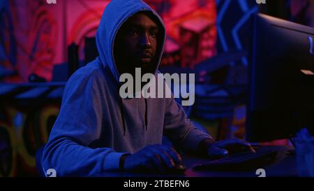 Hacker in secret dark room writing lines of code on computer, developing virus that get past security systems. Evil developer uses PC in hidden bunker, running hacking script Stock Photo