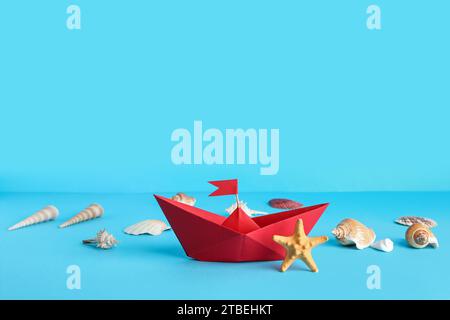 Red origami boat with seashells and starfish on blue background Stock Photo