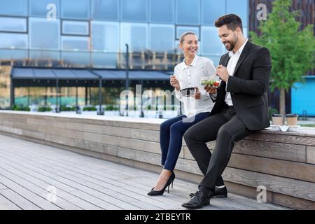 Smiling business people eating from lunch boxes outdoors. Space for text Stock Photo