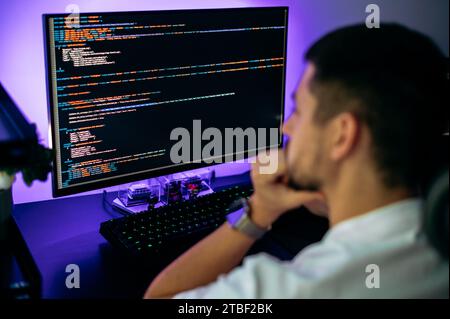 Successful male programmer sits in front of computer screen with programming code abstract technology background of software developer and computer script, working on web resource development Stock Photo