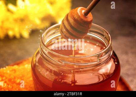 Natural honey dripping from dipper into glass jar under sunlight, closeup Stock Photo
