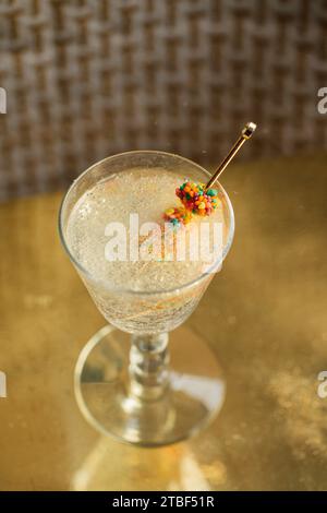 golden cocktail pick in glass of bubbly drink with colorful clusters of candy, reflective metallic gold background Stock Photo