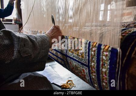 A Kashmiri artisan weaves a traditional carpet at a factory in Srinagar, the summer capital of Jammu and Kashmir. Famed the world over for their resplendent colour and intricate patterns, the carpets woven by the artisans of Jammu & Kashmir hold a centuries old legacy in their weave. The magnificent craft of carpet weaving was brought to the Kashmir valley from Persia in the 14th century. Kashmiri carpets are popular throughout the world for their quality material and authenticity and are specifically known for being handmade and unique in their exquisite style. The continued demand for carpe Stock Photo