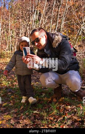 Father and his toddler using mobile phone in the forest Stock Photo