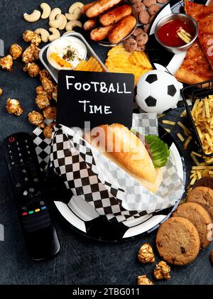 Saturated fats. Football time. TV remote control and snacks - chips, popcorn, cookies, cheese, sauce, fries, burger, nuts. Top view Stock Photo