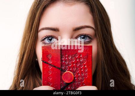 Clutching a diary, her eyes, rimmed with intrigue, invite onlookers to ponder the thoughts hidden behind its pages Stock Photo