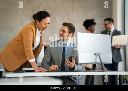Senior business manager talking with experienced colleague while using computer in office. Stock Photo