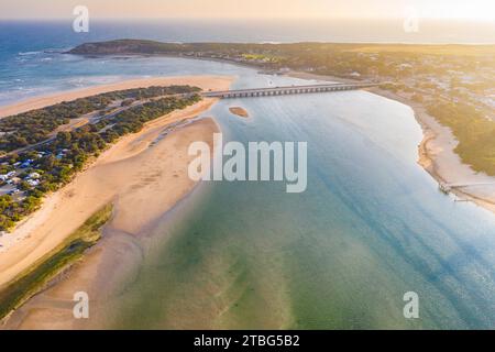 Aerial view of a wide river flowing out to sea under a bridge joining two coastal towns   at Barwon Heads in Victoria, Australia Stock Photo