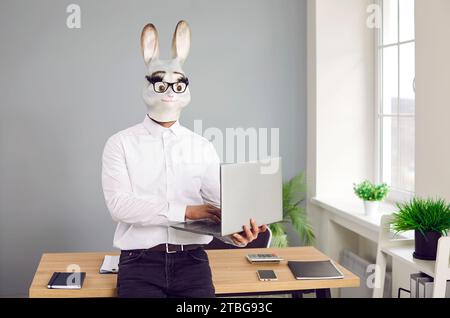 Business man with funny rabbit head standing in office and using laptop computer Stock Photo
