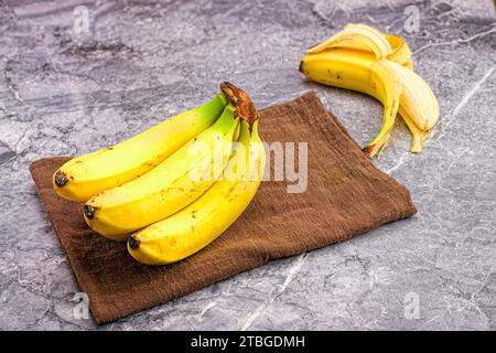 A closeup shot of a cluster of bananas on a brown towel with a peeled one nearby Stock Photo