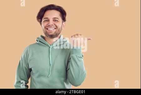 Banner with friendly smiling man in green sweatshirt pointing on copy space on beige background. Stock Photo