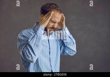 Man who suffers from migraines presses his hands to his head feeling the stress of a headache. Stock Photo