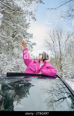 Joyful woman holding a glass of champagne leaning out of the car hatch Stock Photo