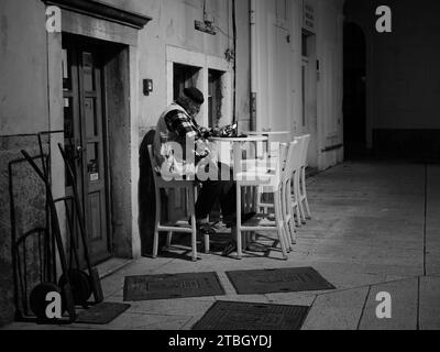 Cres, Croatia - October 23, 2022: Man sitting ouside a bar during night, black and white Stock Photo