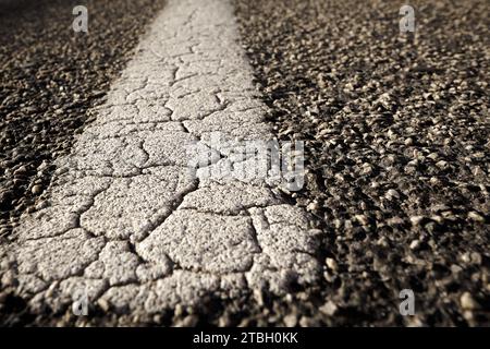 Old dilapidated, cracked road marking on an asphalt road Stock Photo