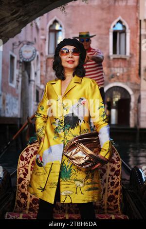 Venice, Italy, a glamourous woman standing in a gondola wearing a gold oriental coat being rowed by venetian gondolier through the beautiful canals. Stock Photo