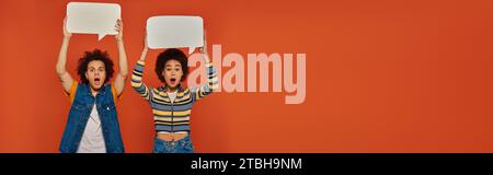 shocked african american brother and sister posing with speech bubbles on orange backdrop, banner Stock Photo