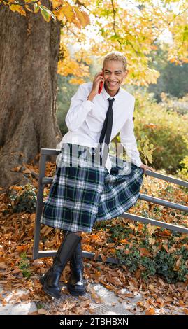 Young man in the park smiling while talking on the cell phone dressed in a kilt, vertical photo Stock Photo