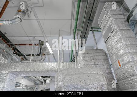 An long ventilation pipe in a technical room of a large building. Air duct, air conditioner pipe on white ceiling wall. Stock Photo