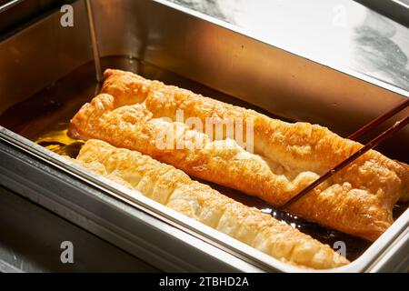 Chinese deep fried dough in hot oil on steel pan. Youtiao, Padnoongo or fried flour sticks is one of the popular breakfasts of Chinese pople, popular Stock Photo