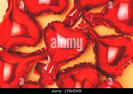 Texture made of red inflatable foil balloons in a heart shape on a gold colored background. Festive concept. Stock Photo