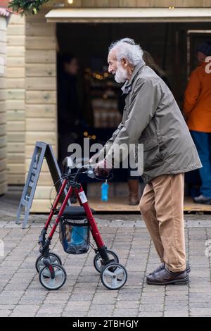 An elderly man using a wheeled walking aid rollator walking through Lemon Quay in Truro in Cornwall in the UK. Stock Photo