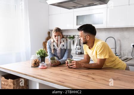 Small talks. Man and woman standing in the kitchen chitchatting while they drinking coffee after female come back home from her workplace. Businesswom Stock Photo